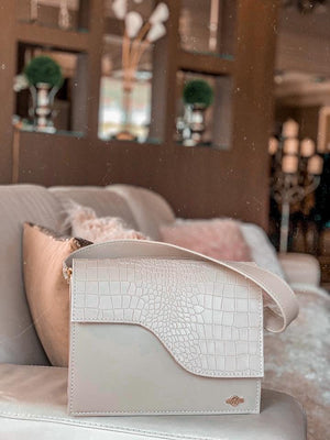 A beige handbag placed on the side of the couch in a room.